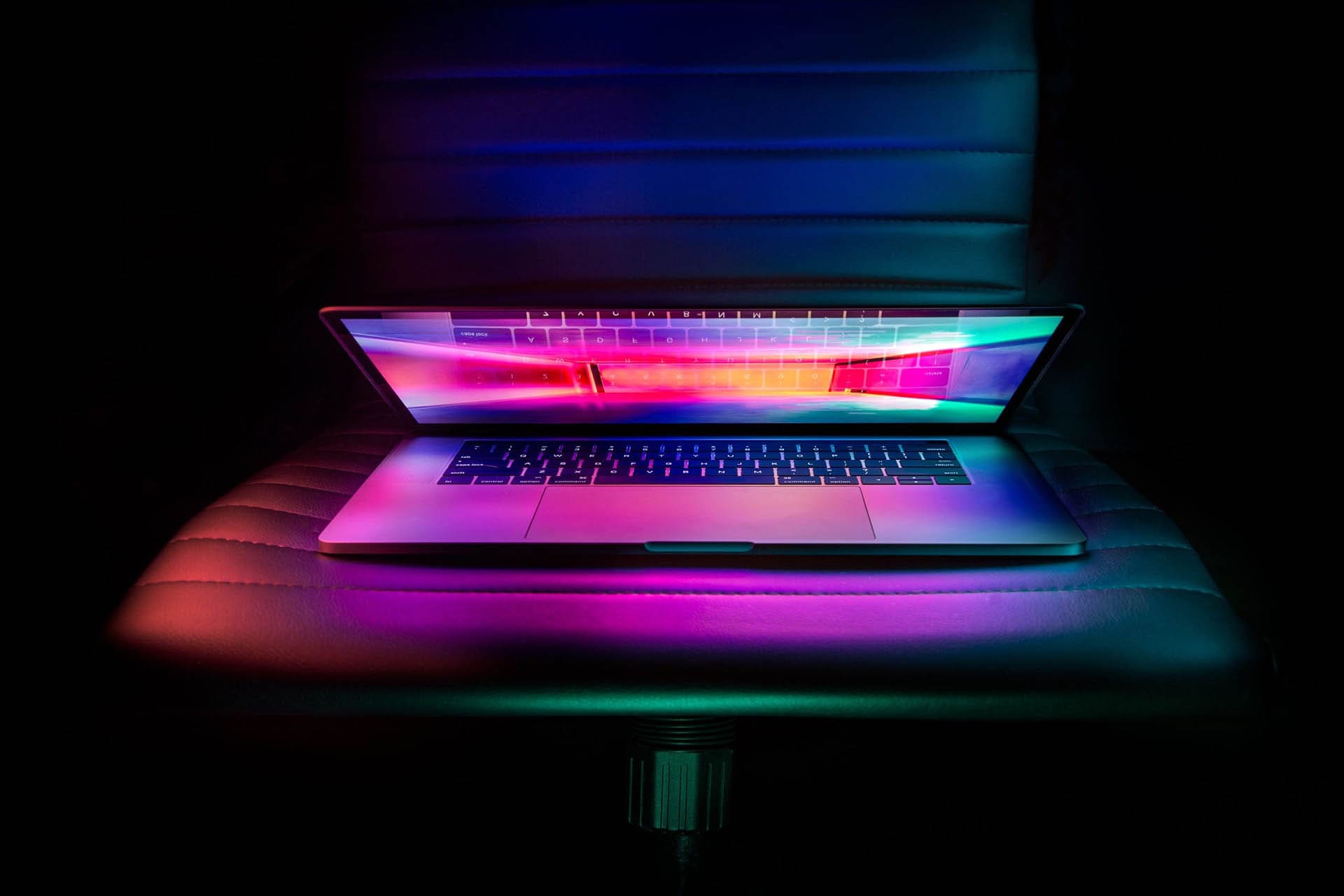 Picture of a laptop with a neon wallpaper sitting on a chair half open in the dark
